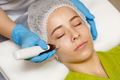 Facial treatment with a gloved technician using a device on a woman’s cheek as she relaxes on a bed