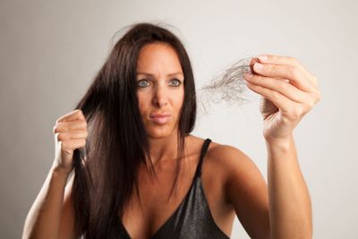 Woman holding a clump of hair in one hand and a hairbrush in the other, looking frustrated.
