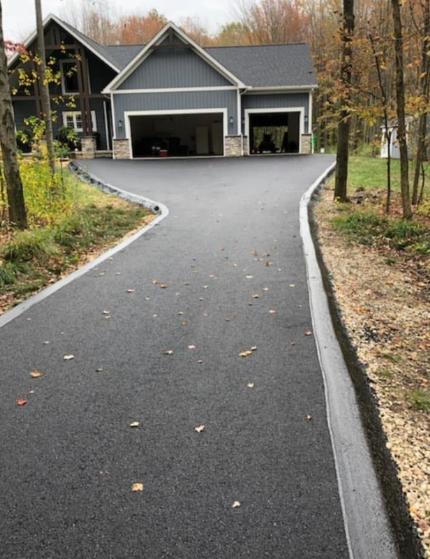 A gray-sided house with a three-car garage and a newly paved asphalt driveway with light-colored concrete curbing.