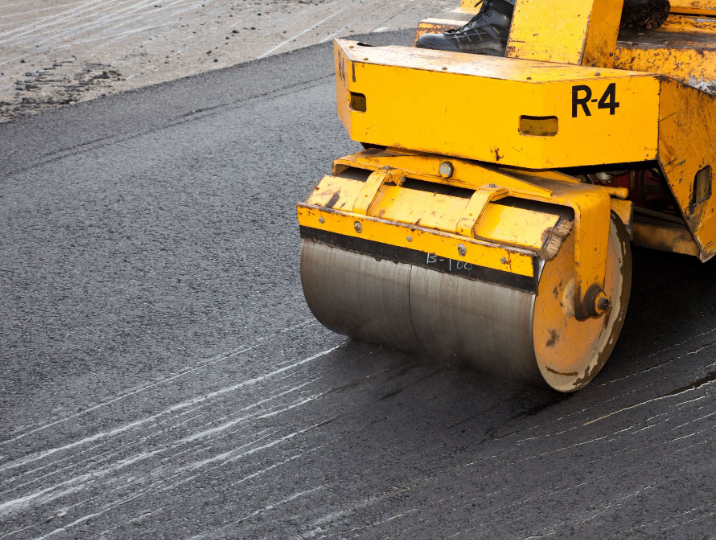 A yellow industrial road roller compacting freshly laid asphalt on a construction site.