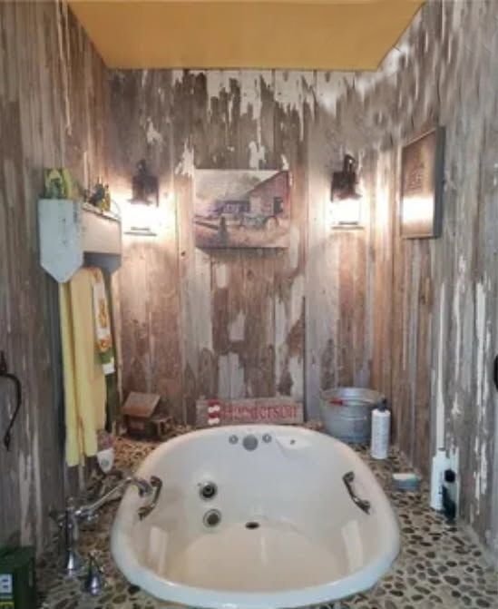 Rustic bathroom with a white jacuzzi tub, wood-paneled walls, and pebble flooring.
