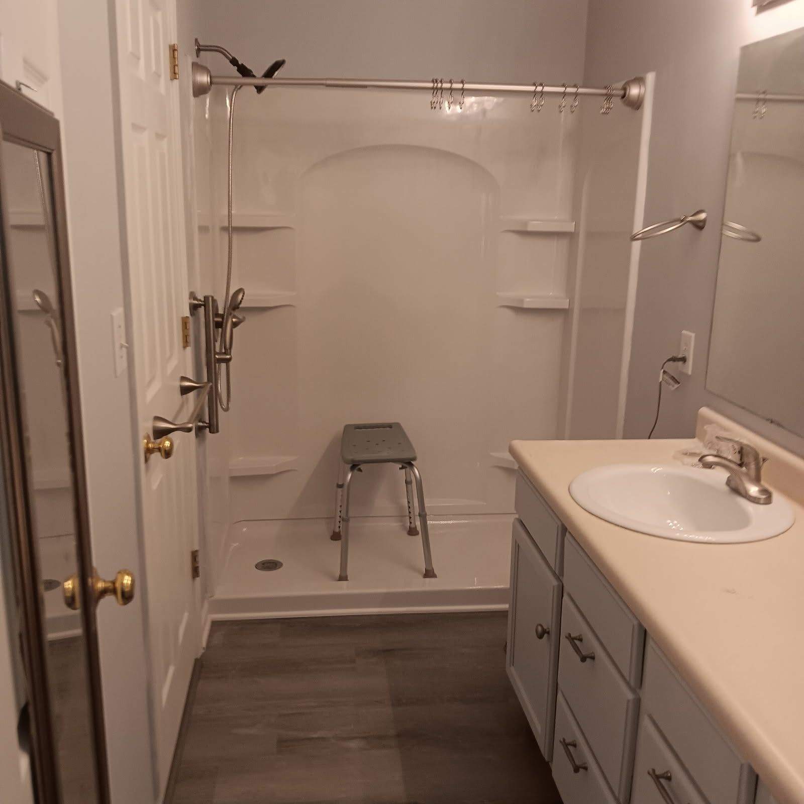 Bathroom with a shower stall, vanity, and a door. Gray walls and wood-look flooring.