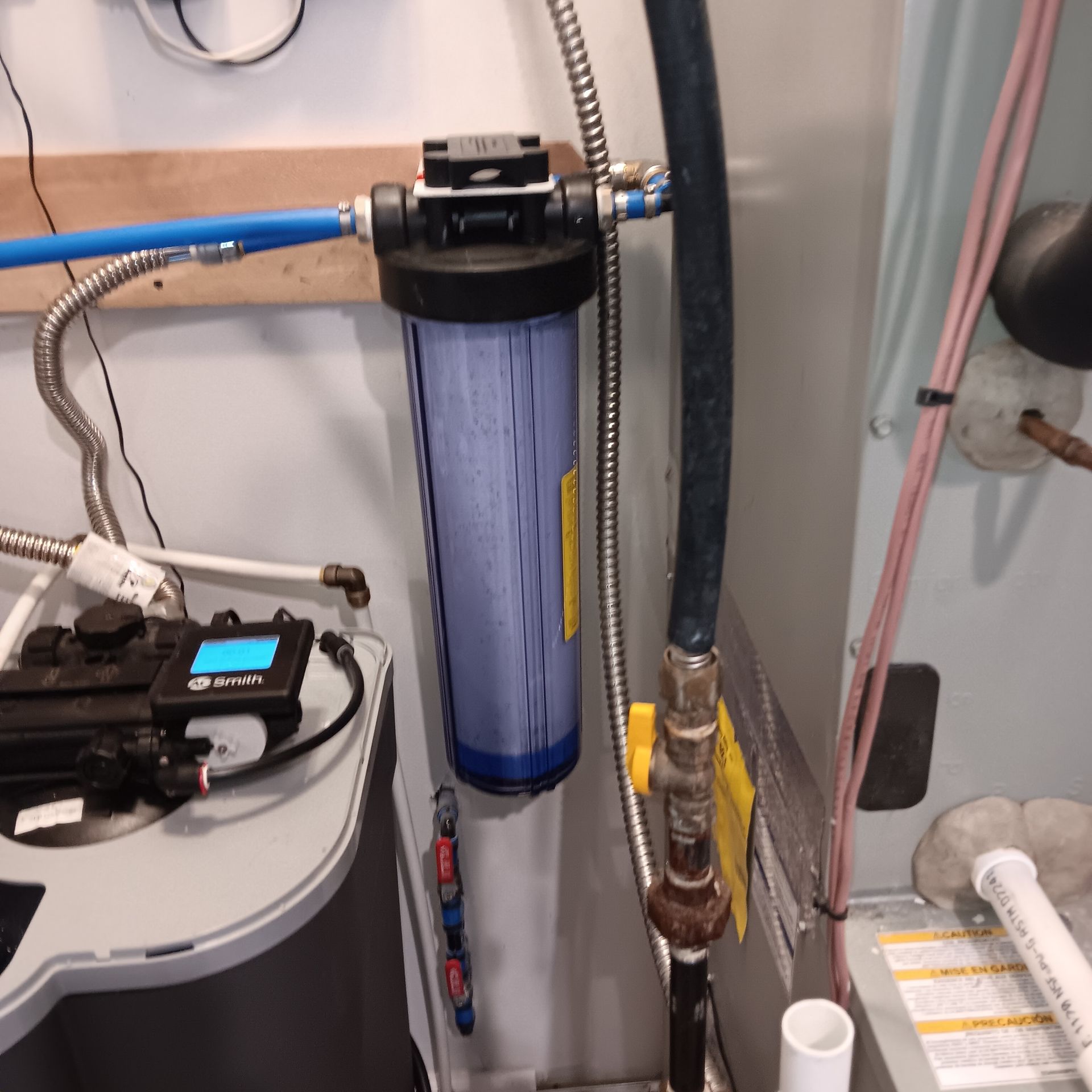 Water filter system with blue canister, pipes, and control panel on a wall.