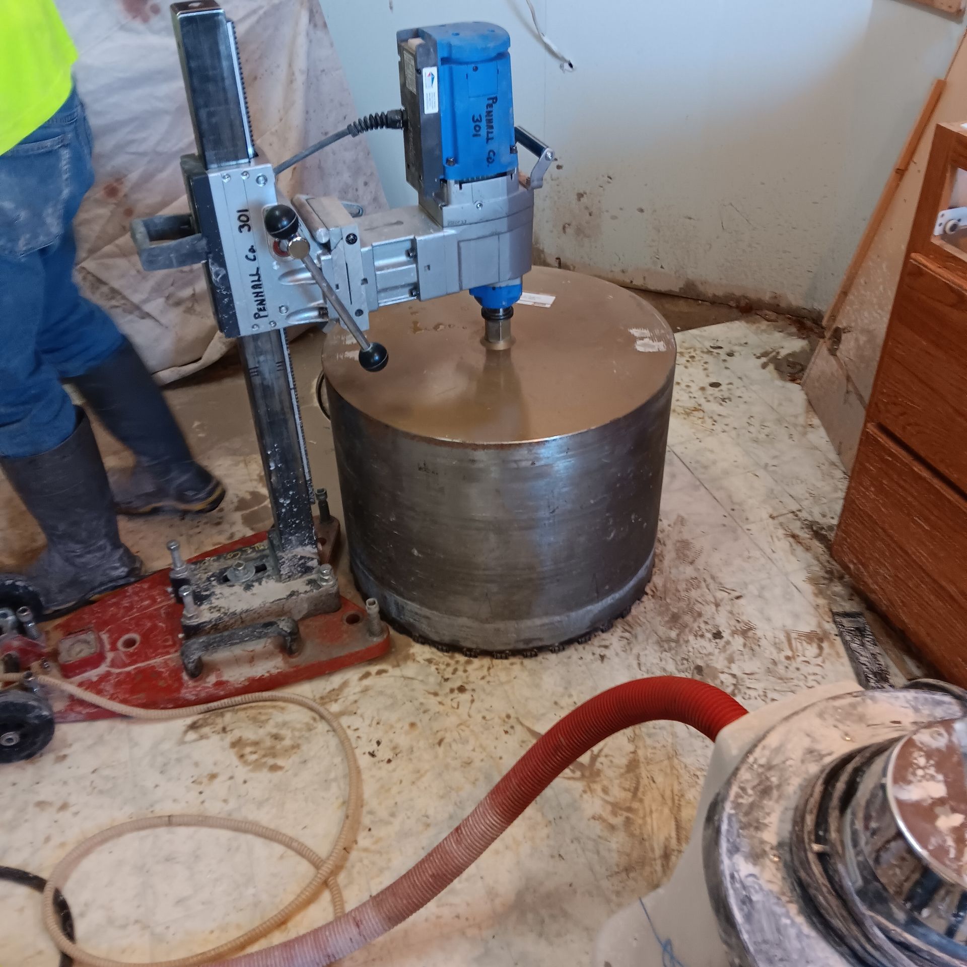A concrete core drilling machine in use, cutting a large hole in a concrete floor inside a building.