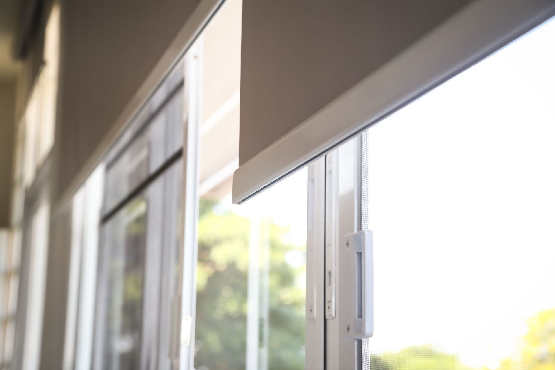 Roller shade partially drawn over a sliding glass door, white frame, bright sunlight.