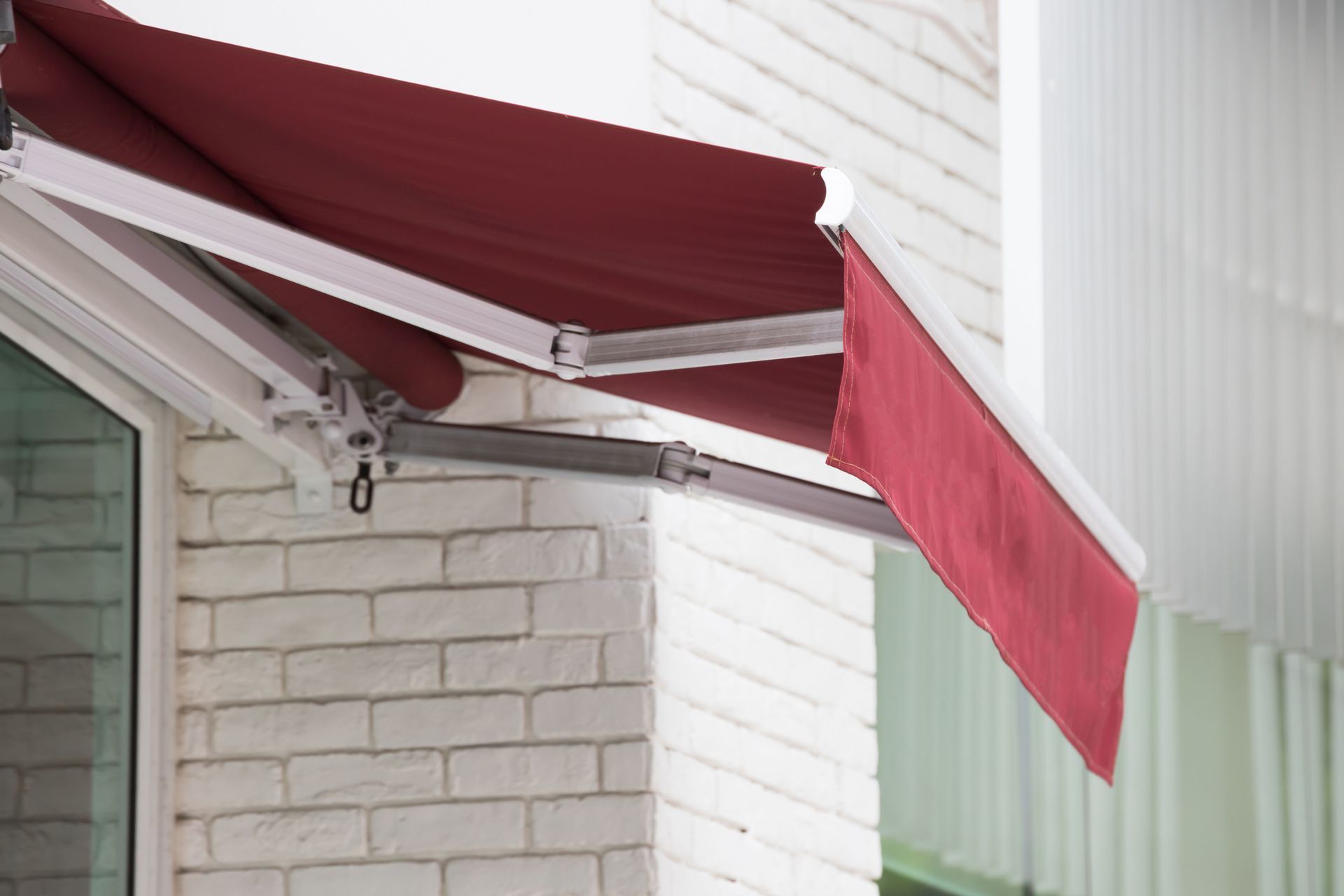 A deep red retractable fabric awning mounted over a white brick wall and a window.