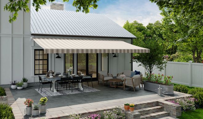 Back patio with outdoor dining table, wicker seating, potted plants, and an awning beside a white house