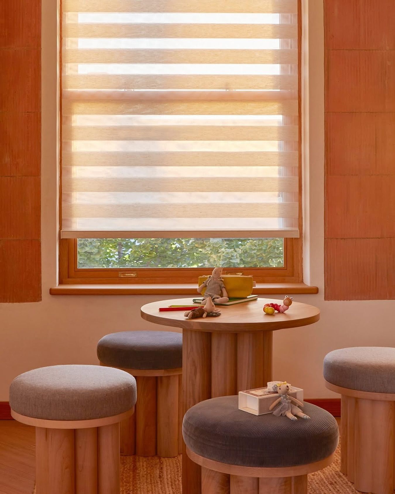 Window with striped shade; small round table with stools. Room with warm tones.
