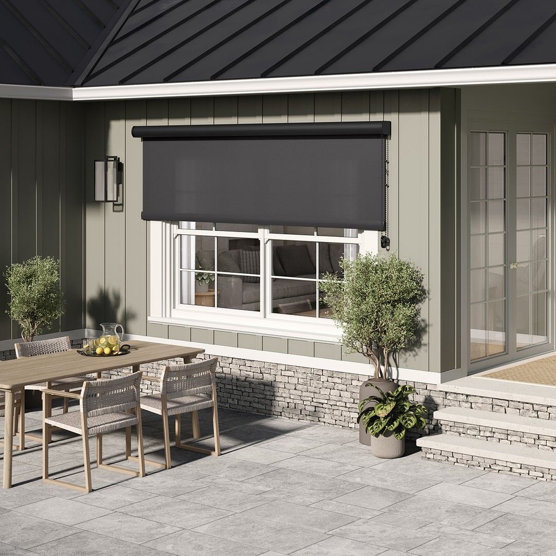 Exterior patio with gray shade over a window, table, chairs, plants.