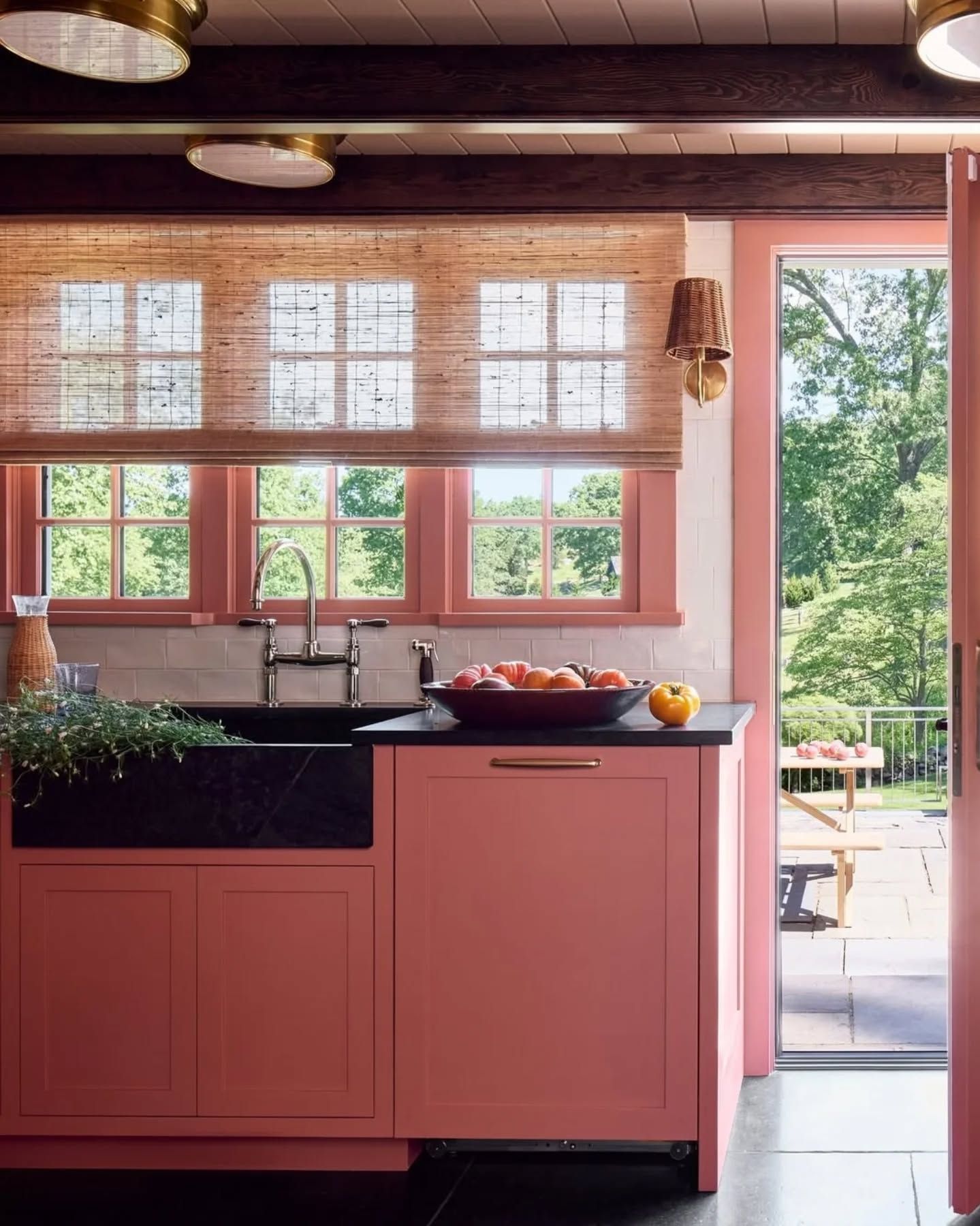 Pink kitchen with black sink, peach accents, and open doorway to a sunny backyard.