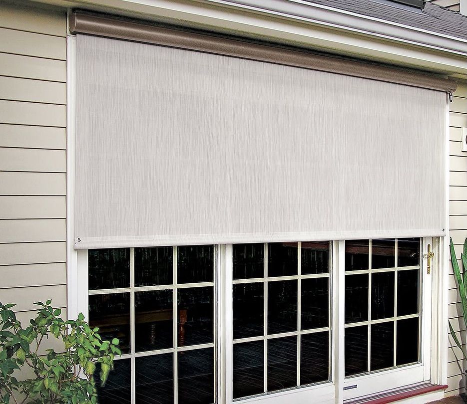 Beige outdoor shade covering a glass door, attached to a home's exterior.
