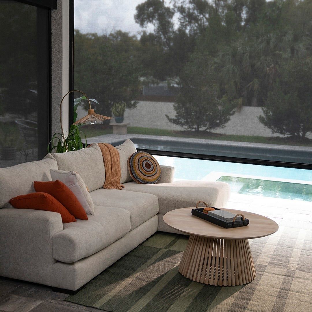 Lounge area by a pool with a white sofa, orange pillows, and a wooden coffee table.