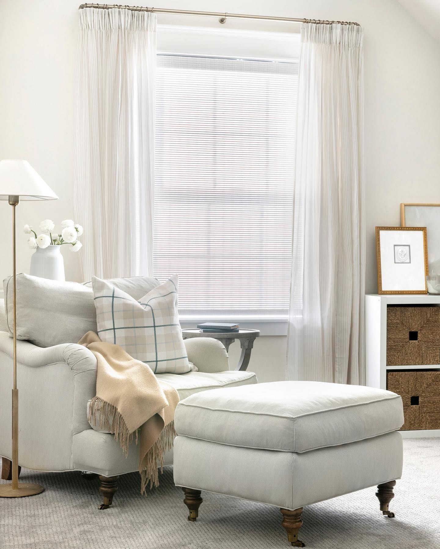 Cozy reading nook with a cushioned armchair and ottoman by a window with sheer curtains.