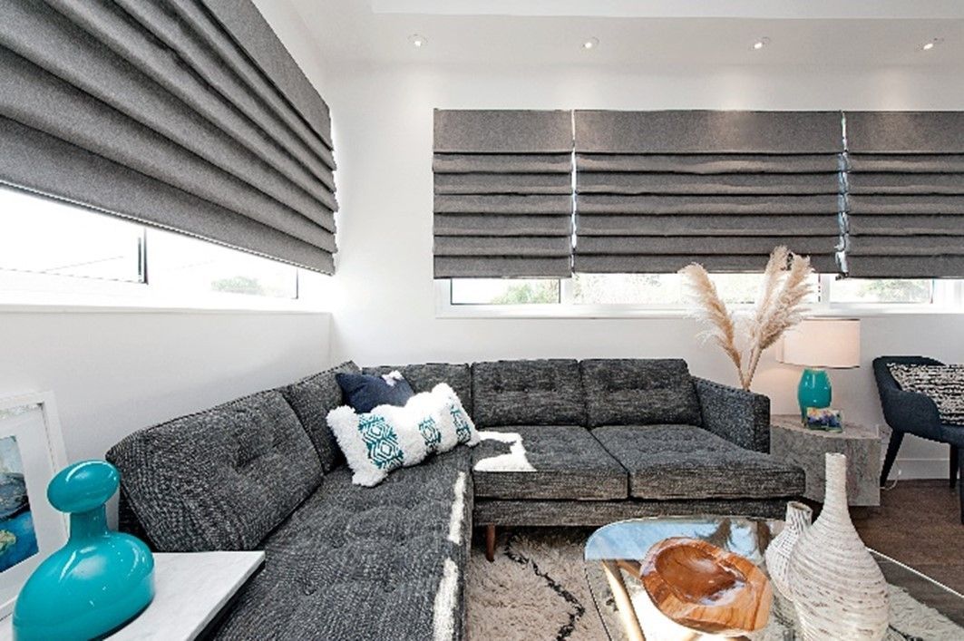 Gray sectional sofa in a bright living room with gray Roman shades and accent decor.