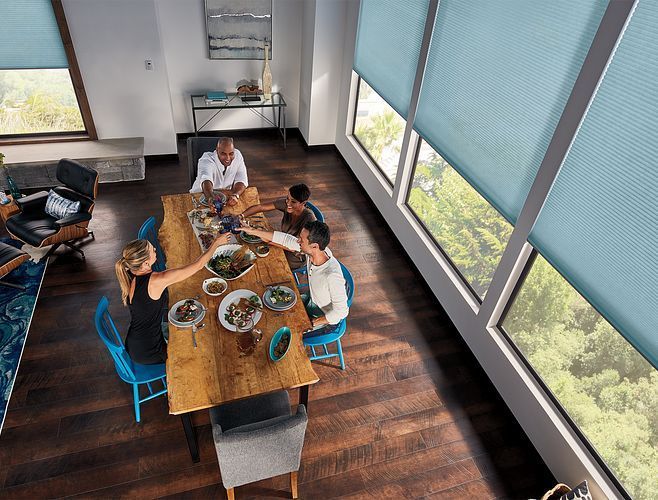People toasting around a wooden dining table. Blue chairs. Large windows with blue shades.