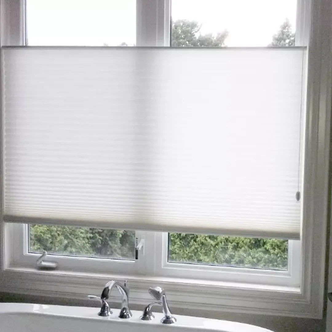 White cellular shade on a window above a bathtub, partially covering the view.