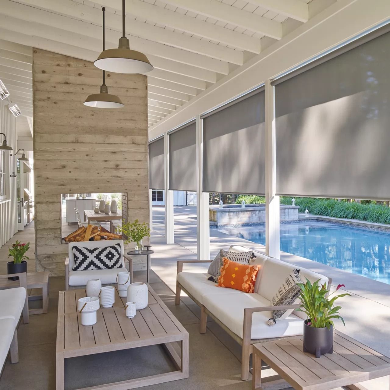 Outdoor living space with gray roll-down shades, a fireplace, furniture, and a pool.