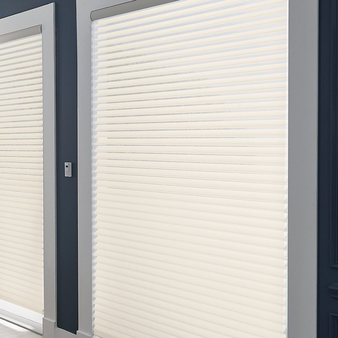 Two white pleated window shades against a blue wall.