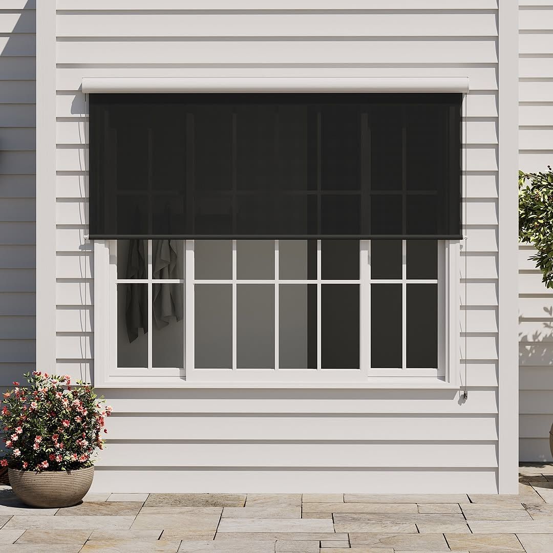 Black mesh shade covers a white window on a white clapboard house. A potted plant sits in front.