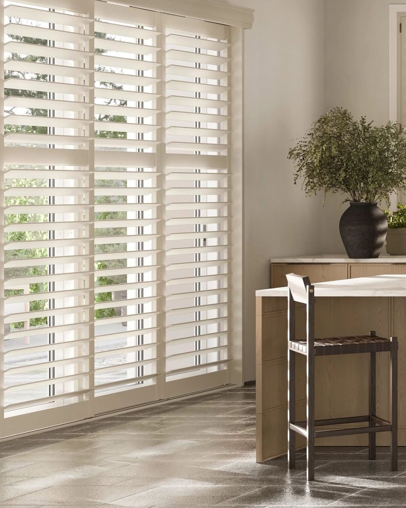 Sliding glass door with white shutters in a kitchen; a tall vase with greenery and a bar stool are visible.