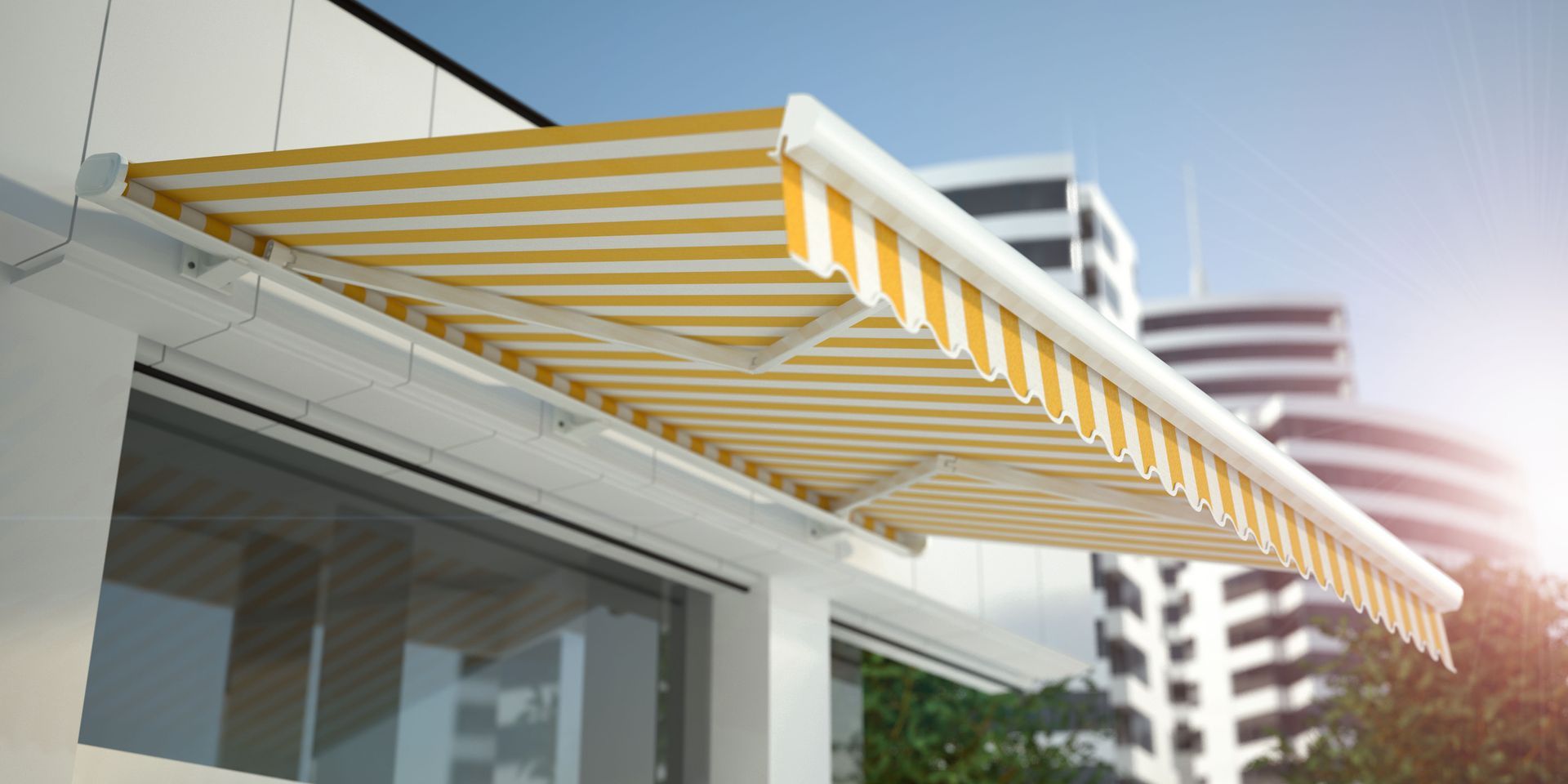 A retractable striped yellow and white awning mounted over a building window with a city building in the background.