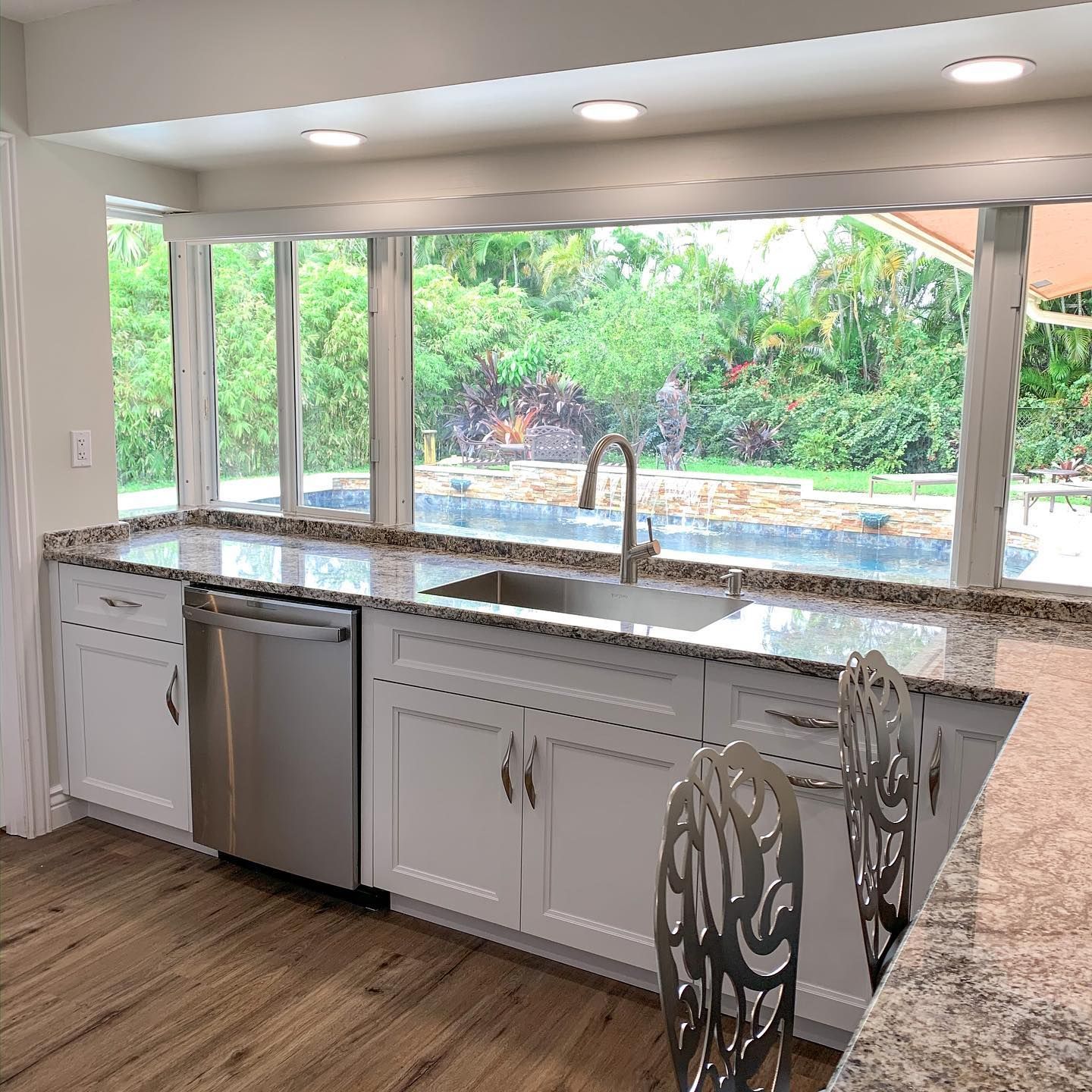 A kitchen with white cabinets , granite counter tops , stainless steel appliances and a large window.