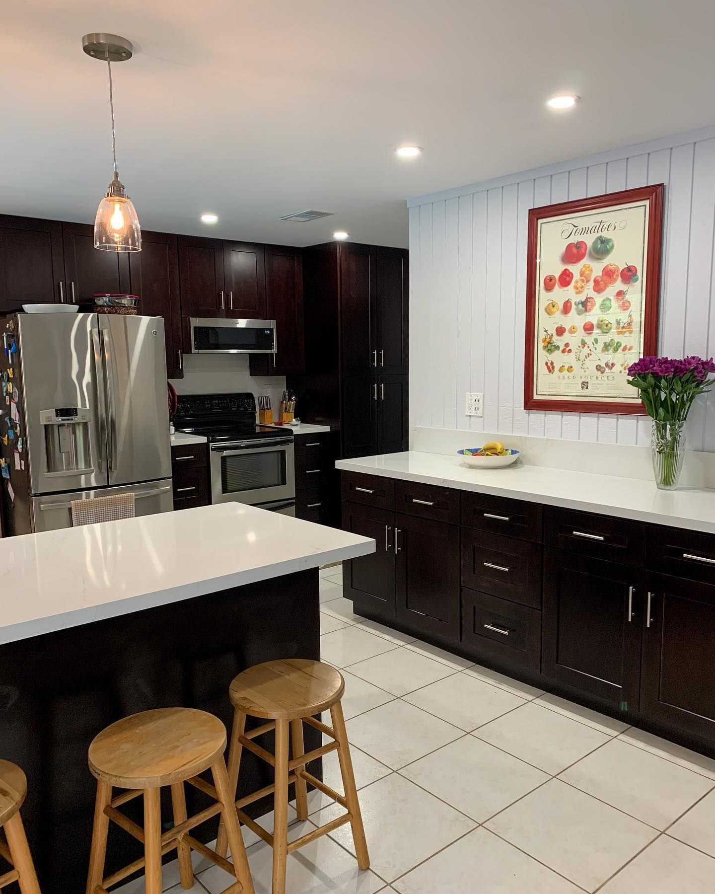A kitchen with stools , a refrigerator , a stove , and a picture on the wall.