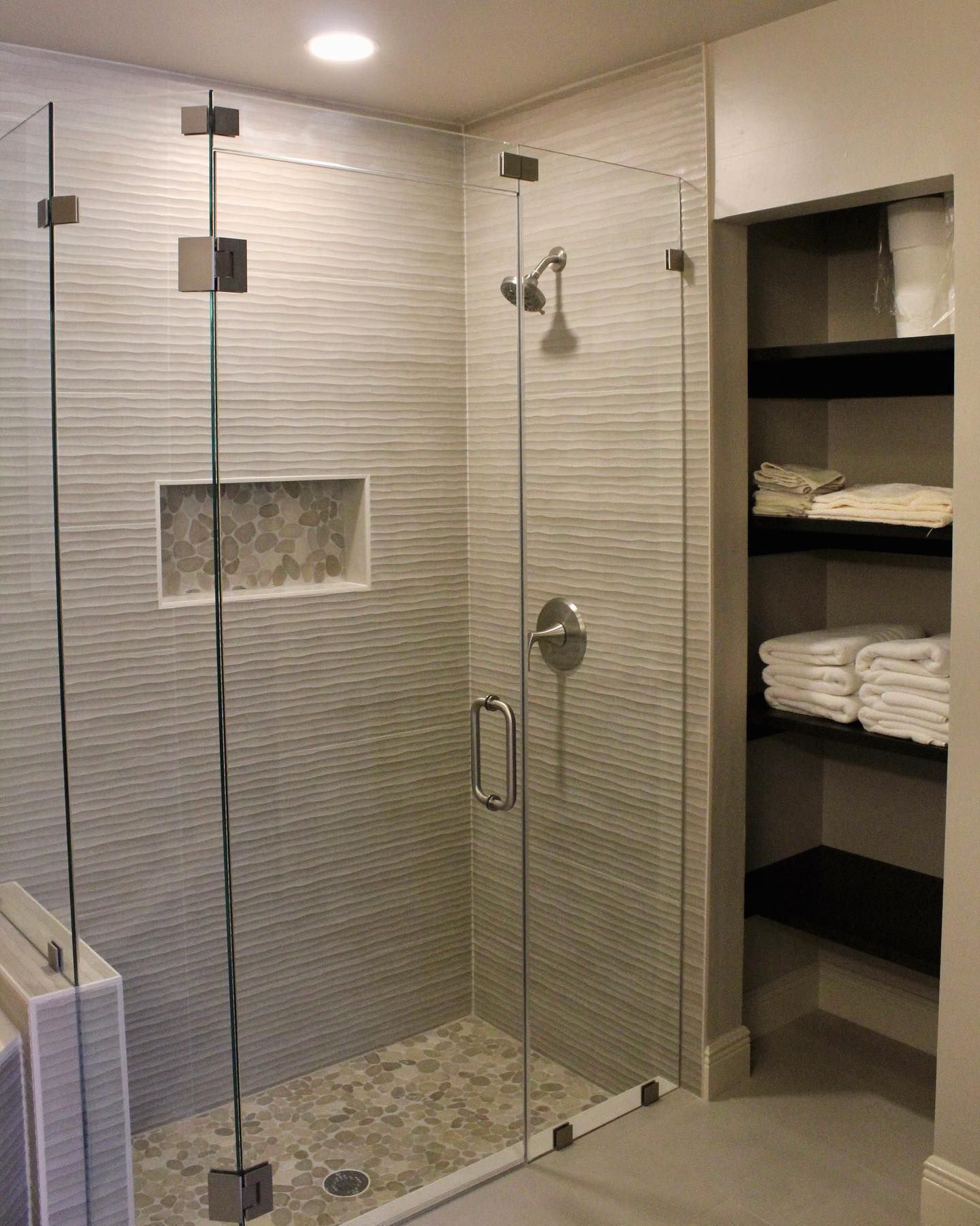 A bathroom with a walk in shower and a closet filled with towels.