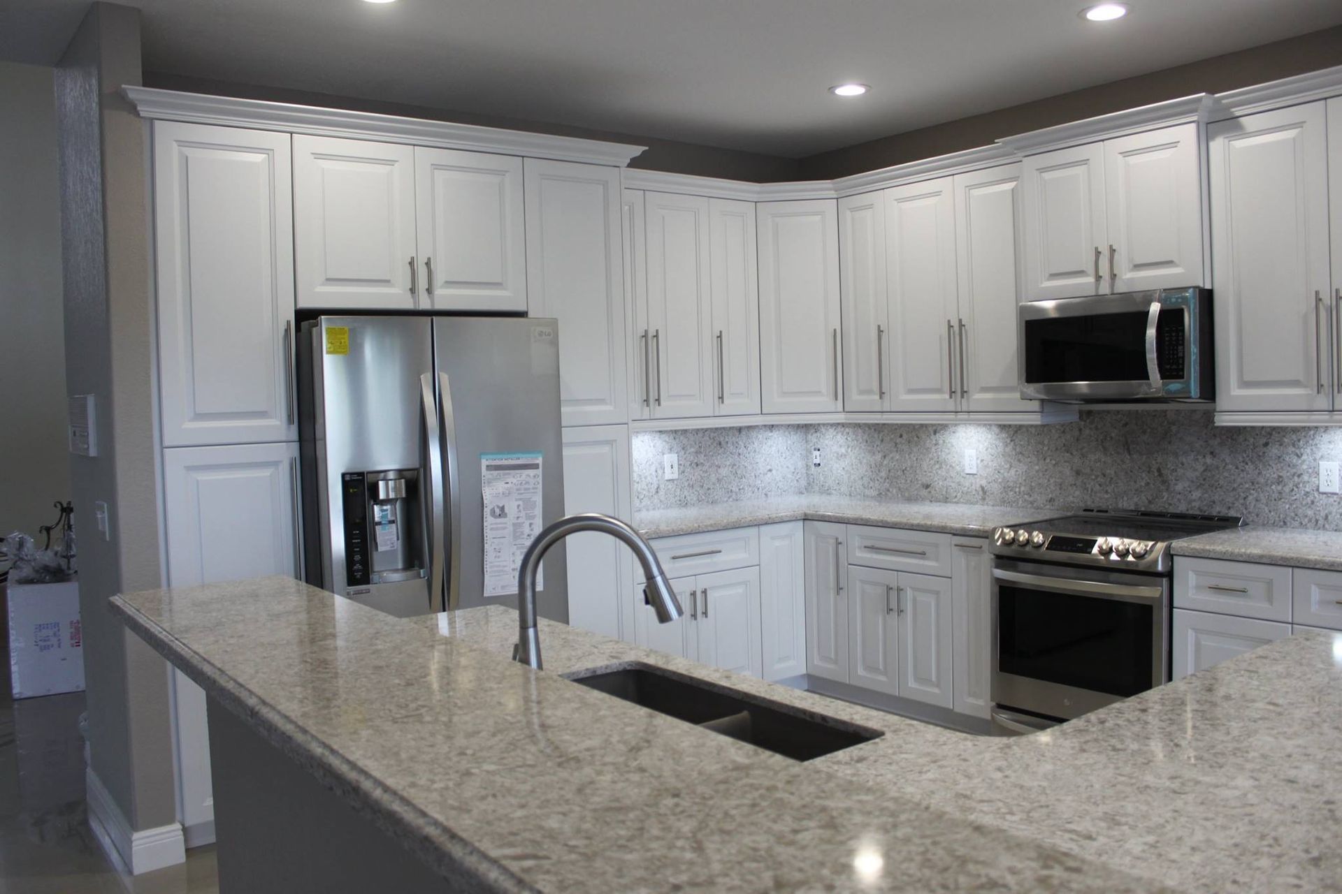 A kitchen with white cabinets , granite counter tops , stainless steel appliances and a refrigerator.