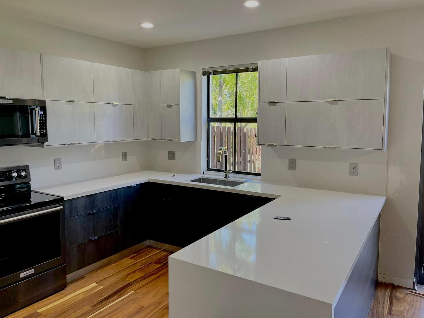 A kitchen with white cabinets , black appliances , a sink , and a window.