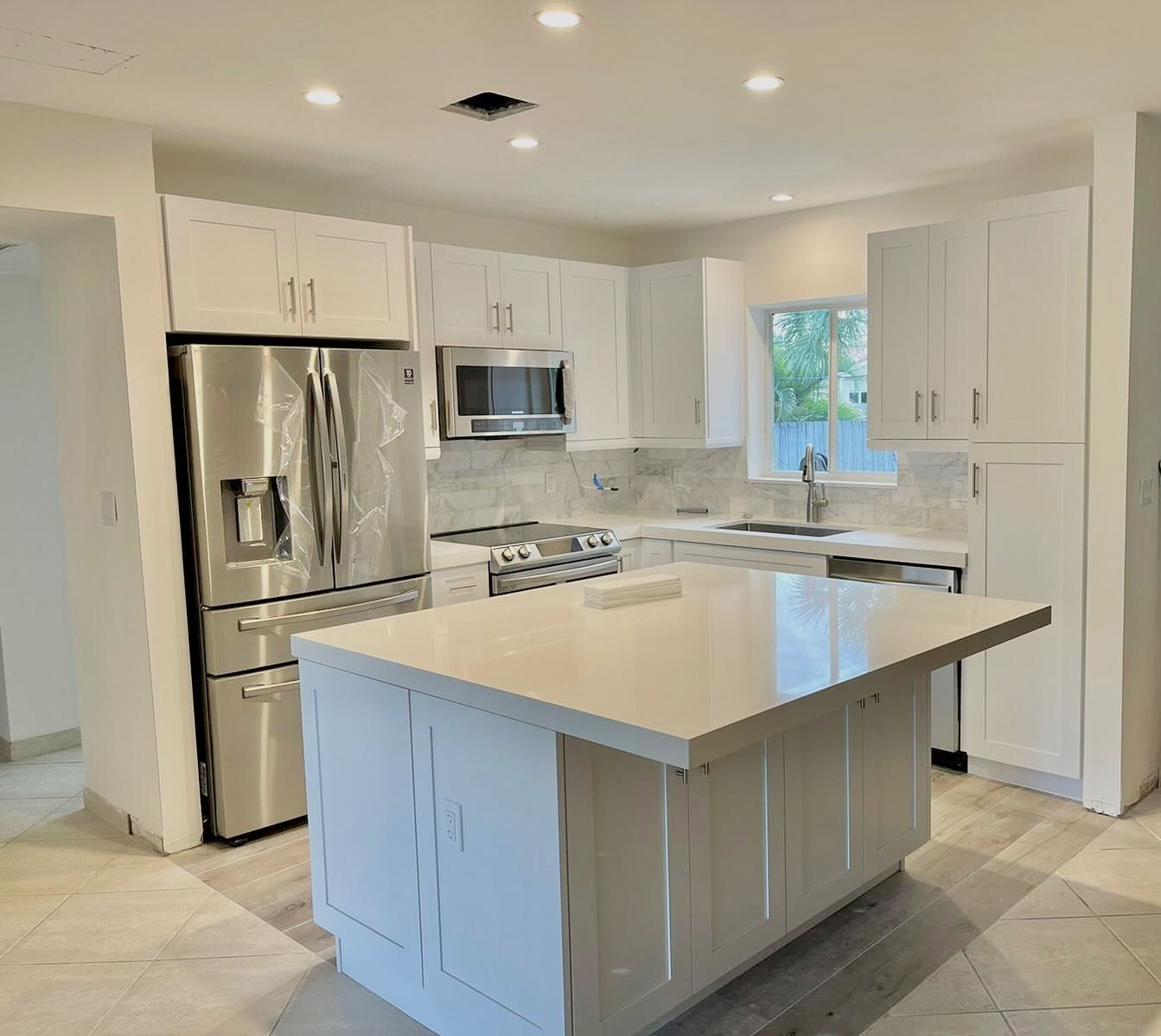 A kitchen with white cabinets , stainless steel appliances , and a large island.