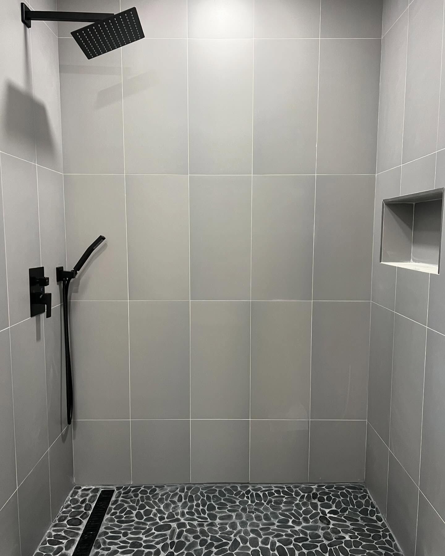 A shower with a black shower head and a black drain.