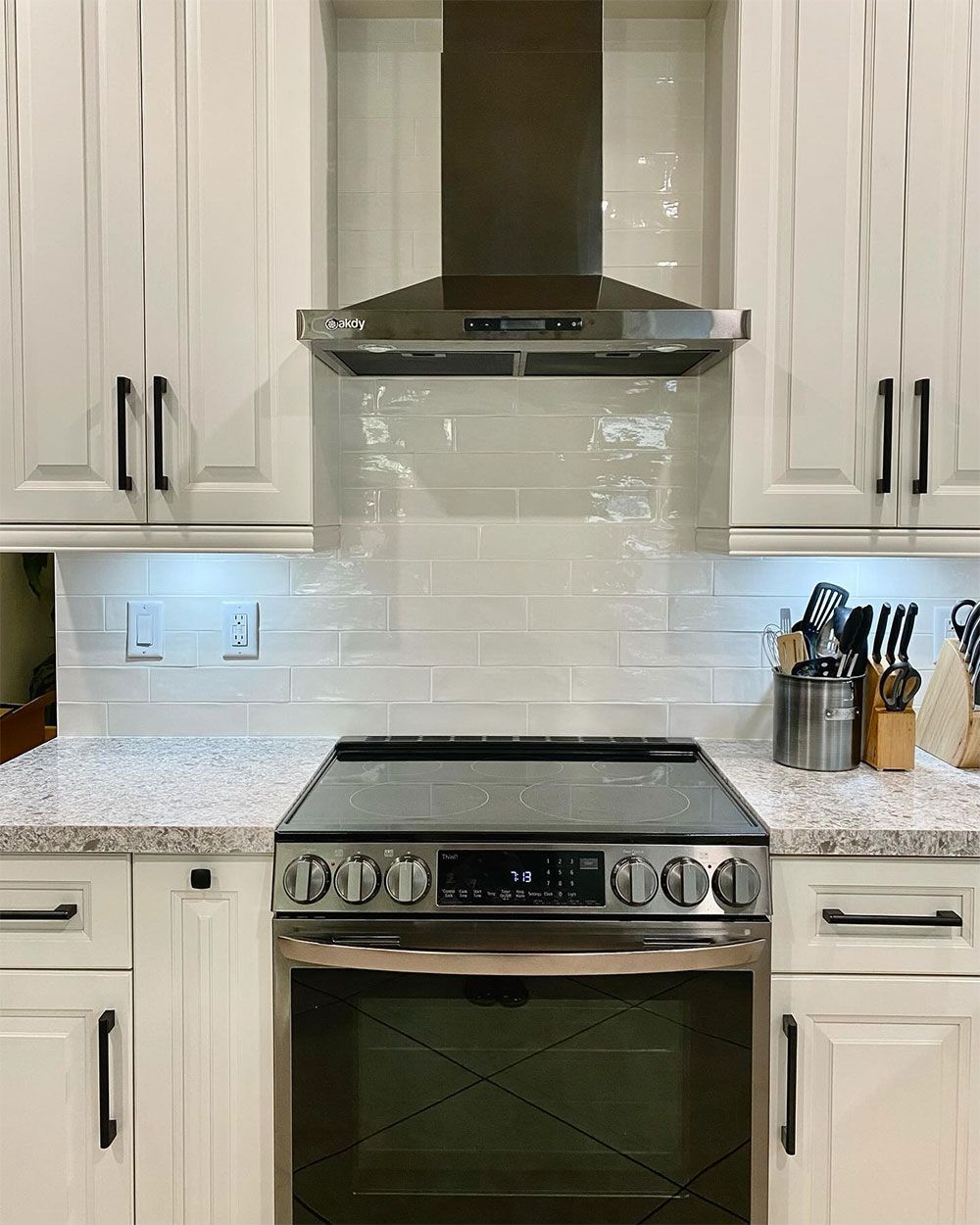 A kitchen with white cabinets , a stove , and a hood.