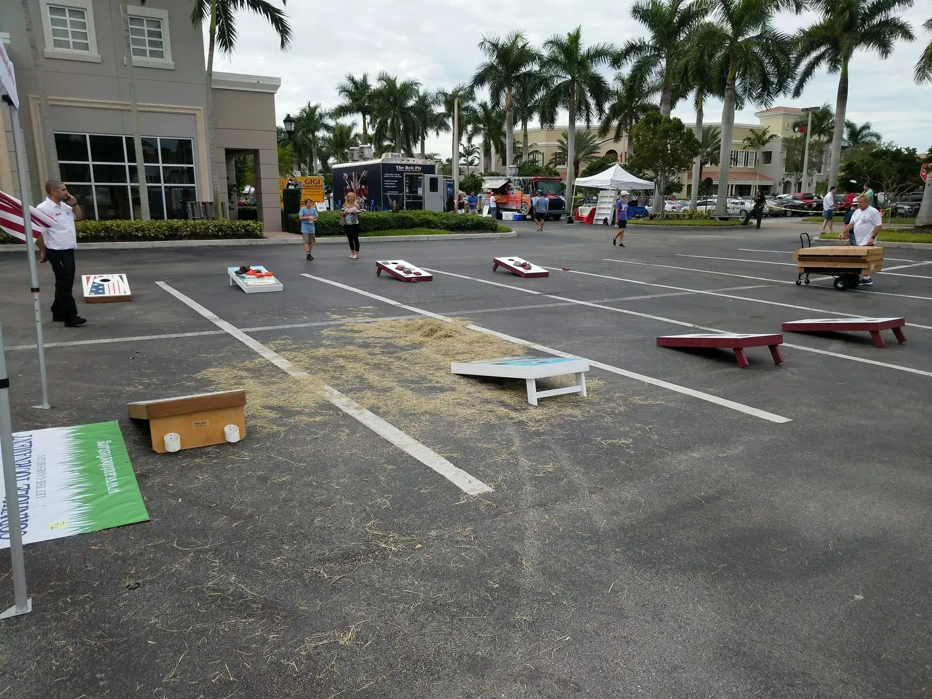 Cornhole boards set up in a parking lot with palm trees and tents in the background.