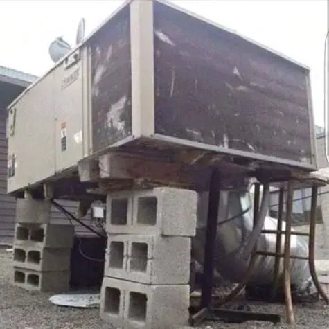 Large industrial HVAC unit on cinder blocks with exposed pipes and support frame outdoors