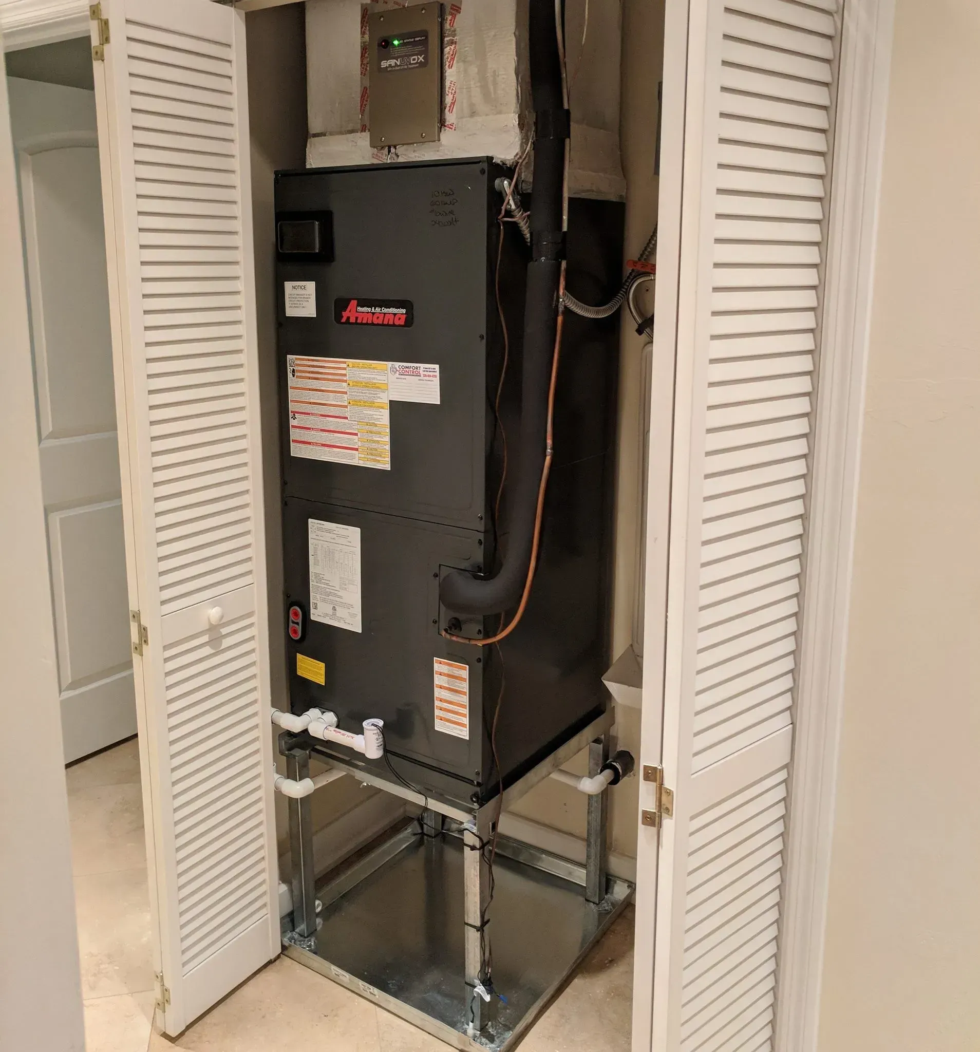 Black HVAC furnace in a hallway closet with open louvered doors and exposed ductwork piping