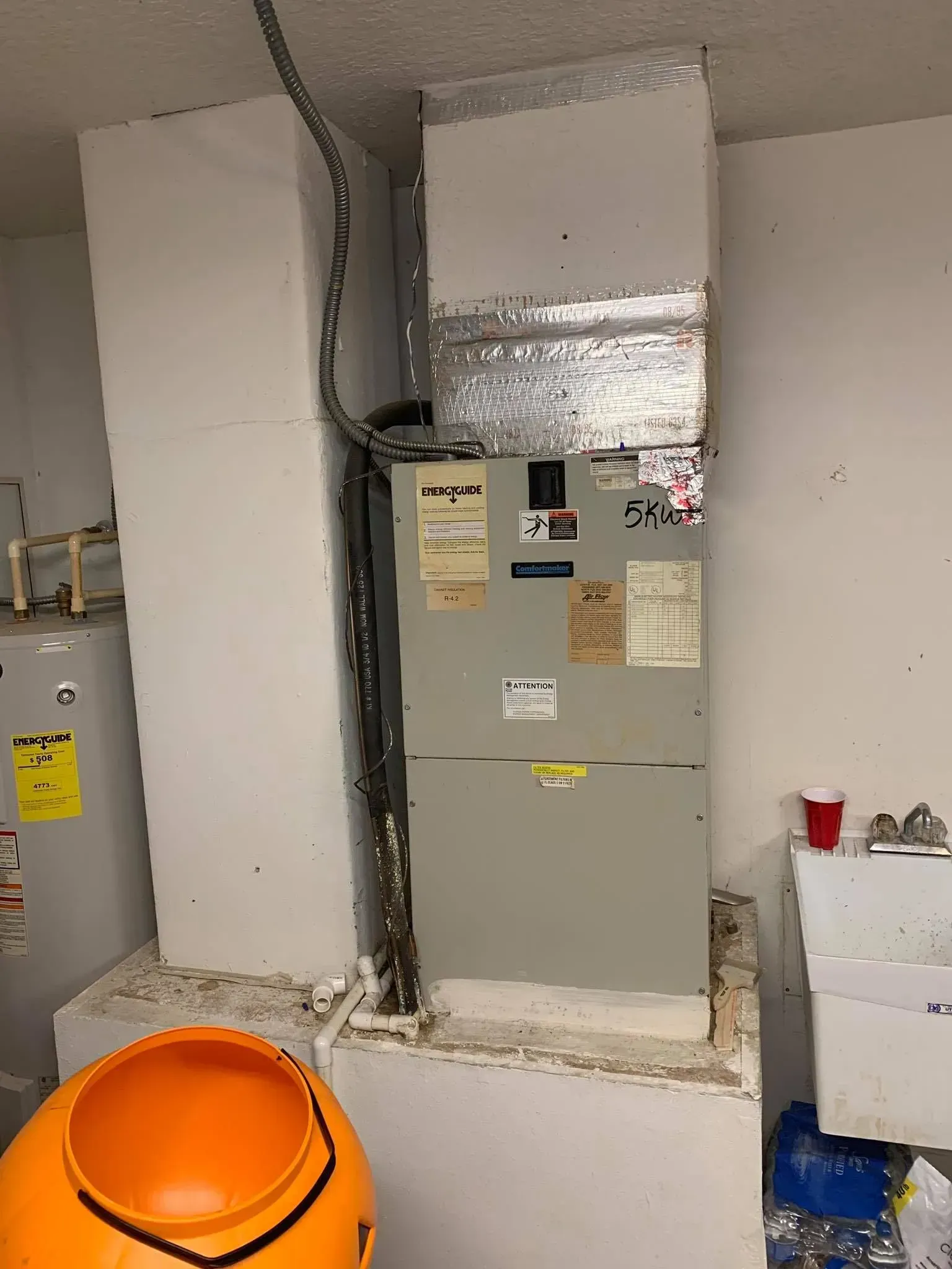Utility room with electrical panel, ducts, and an orange construction bucket in the foreground