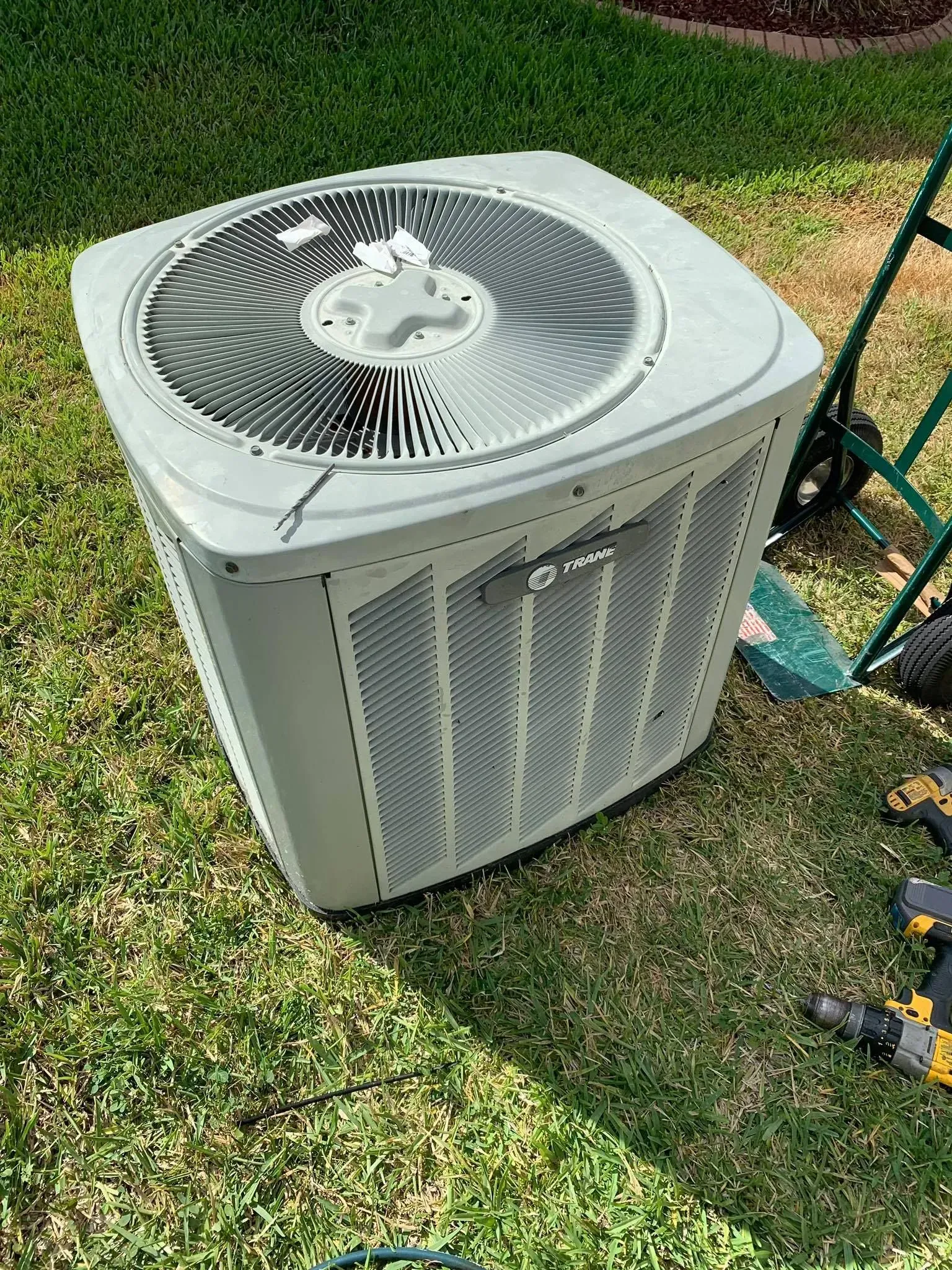 Outdoor air conditioner unit on grass beside a garden path, with a fan grille on top.