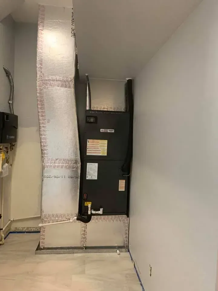 Narrow utility room with HVAC unit, silver ductwork, and white walls and floor.