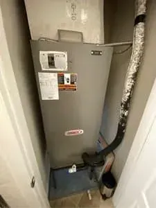 Large HVAC unit in a narrow closet with pipes and ductwork beside it.