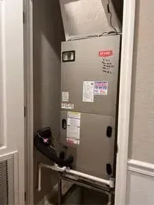 Indoor utility closet with a gray HVAC/furnace unit and exposed ducts behind louvered doors.