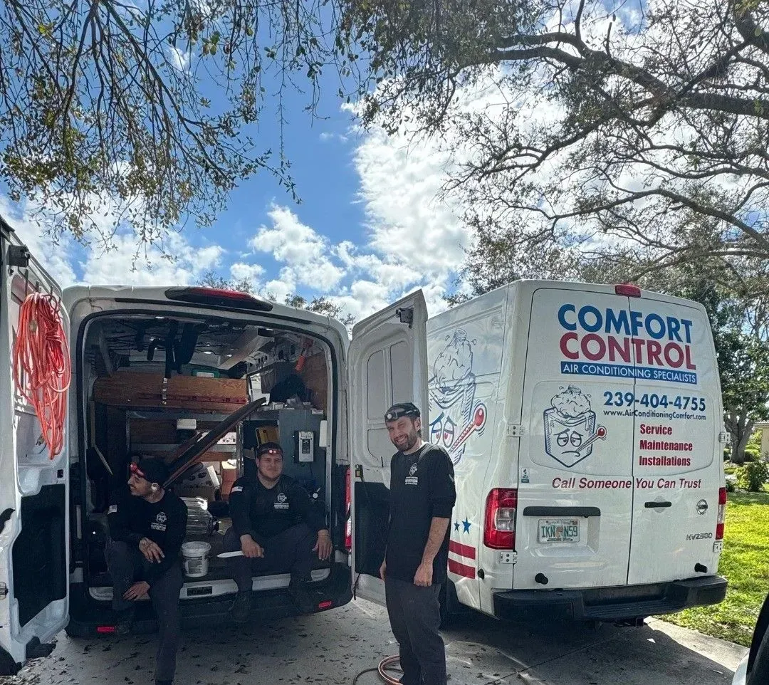 Two white Comfort Control vans parked outdoors, with one open and a man standing between them.