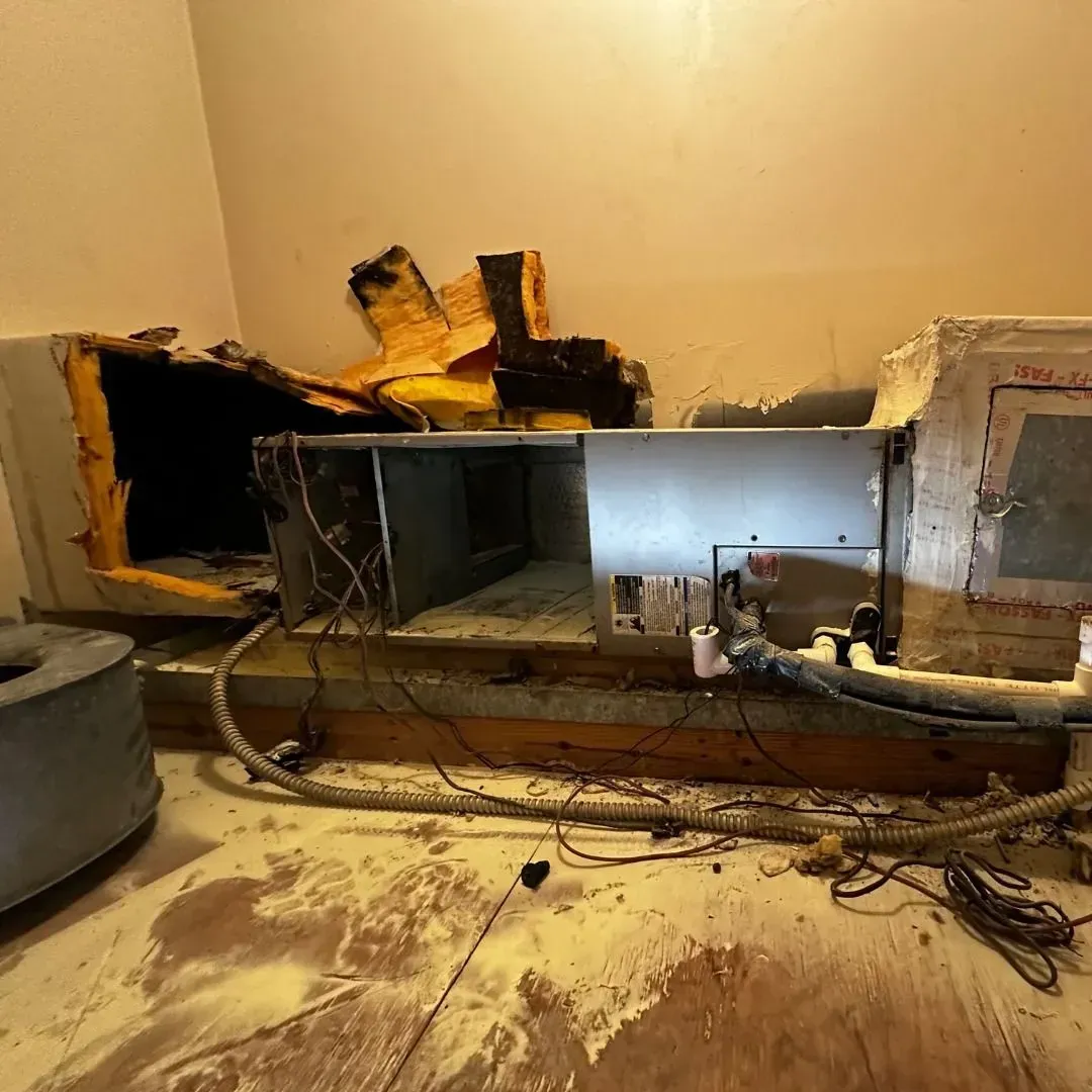 Damaged wall with exposed pipes and wiring, debris scattered on the floor in a room under repair