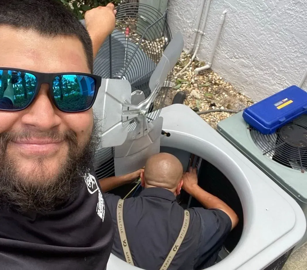 Selfie of a man in sunglasses beside a worker in a gray utility bucket truck.