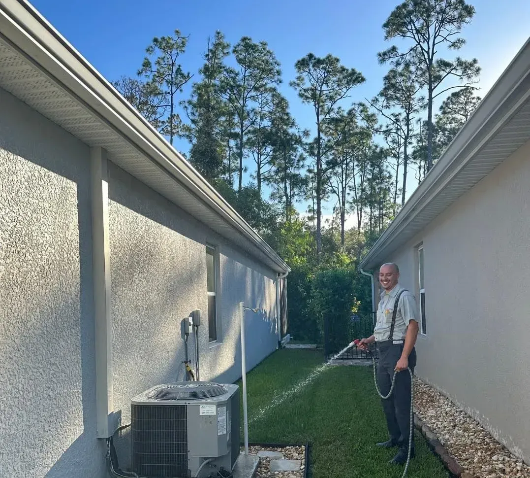 Man using a pressure washer beside a house between two stucco walls on a sunny day