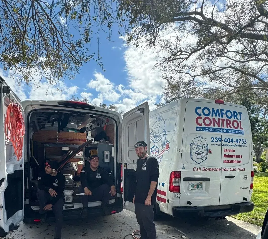 Workers stand between open Comfort Control service vans under a blue sky.