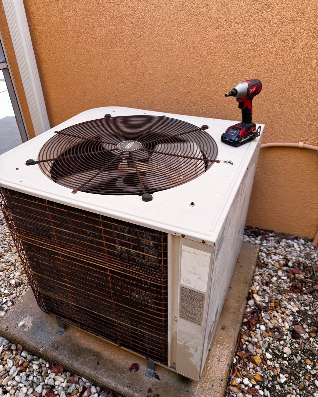 Outdoor air conditioner unit with a fan top and a red-and-black cordless drill sitting on it.