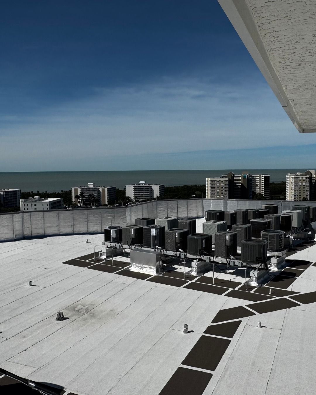 Rooftop HVAC units under a blue sky, with the ocean and distant buildings in view.
