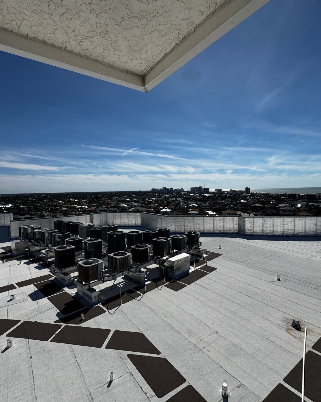 Rooftop HVAC units under a blue sky, viewed over a flat white roof and distant city skyline.