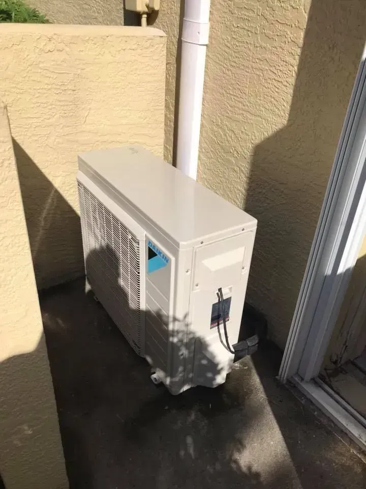 Outdoor wall-mounted air conditioner unit beside a sliding glass door on a patio.